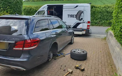 A wheel being changed on a customer's driveway, with our van behind