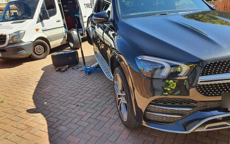 An SUV having a wheel changed on a driveway, with our van alongside