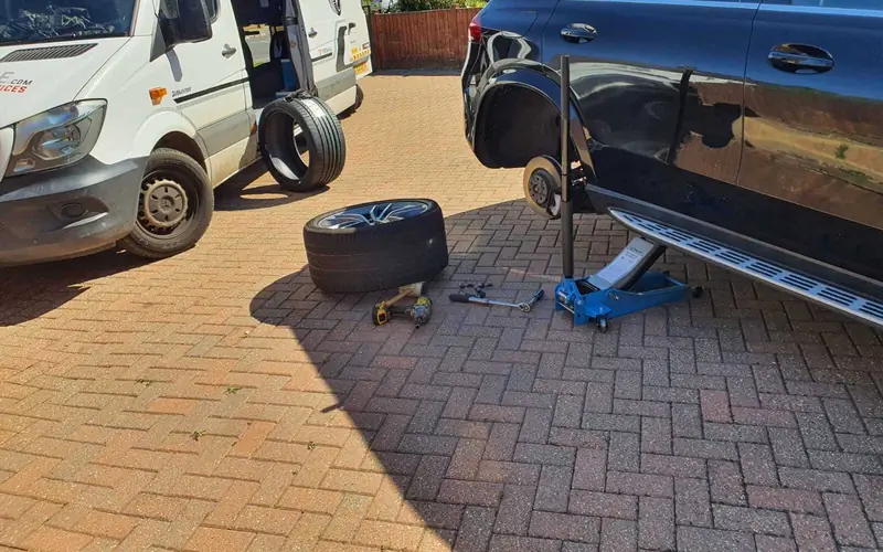 A wheel off and the car on a jack during a mobile tyre job on a driveway
