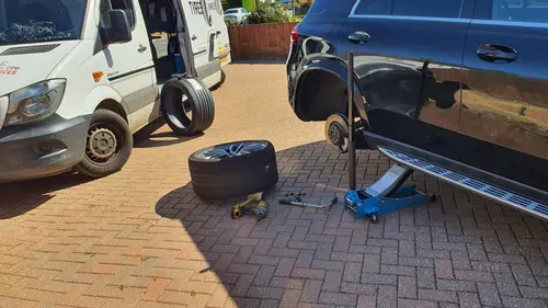 A car on a jack with one wheel removed during a mobile tyre fitting