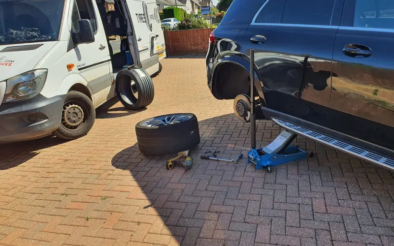 A car on a jack with one wheel removed during a mobile tyre fitting