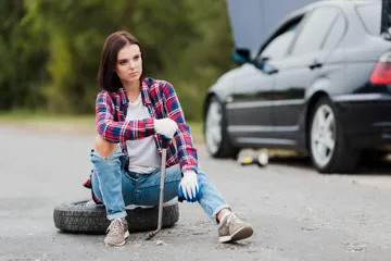 Woman putting a spare tyre on her car on the roadside